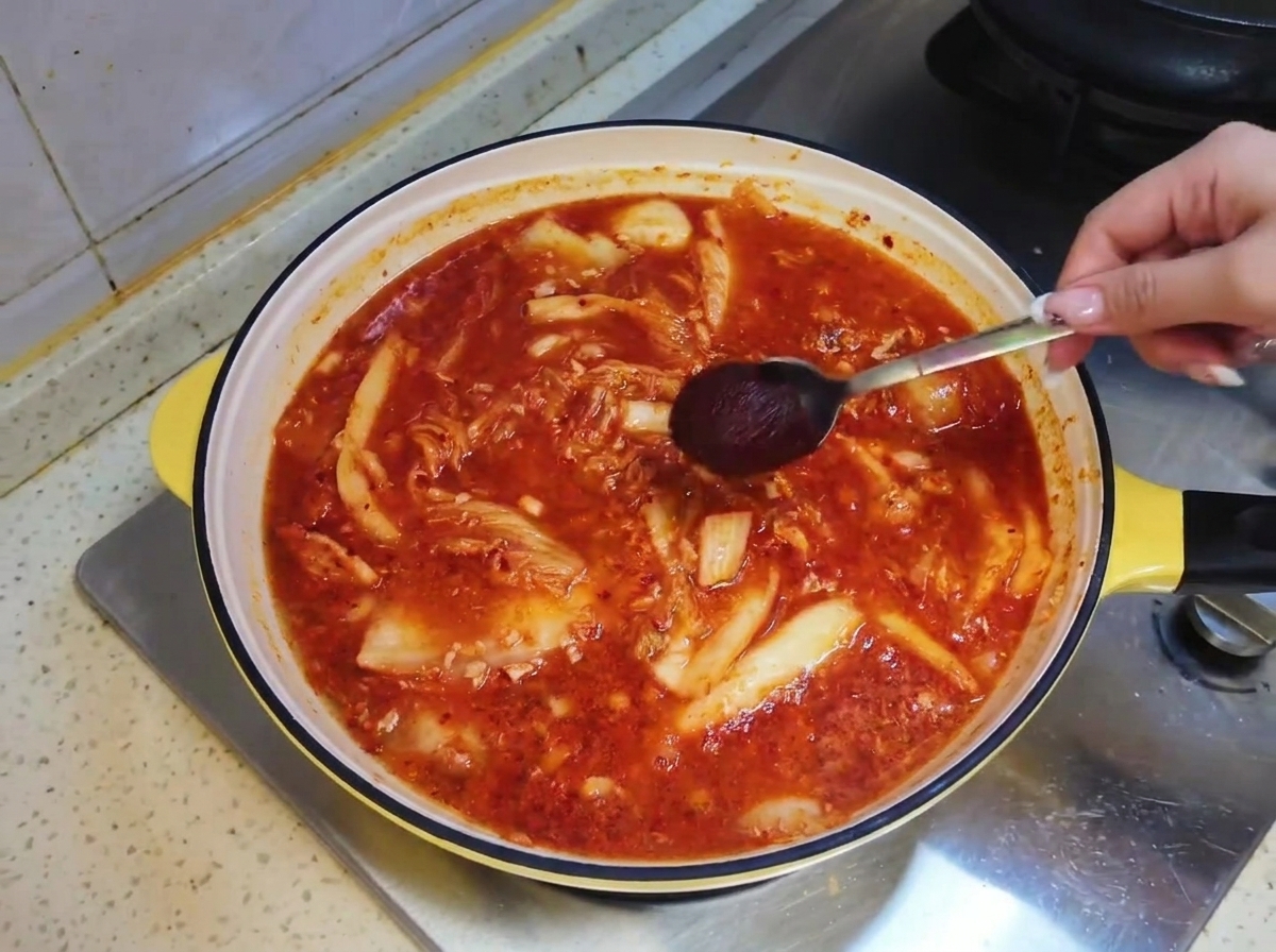 Ein Löffel koreanische scharfe Soße wird in die rötliche Suppenbrühe in der Pfanne getaucht.