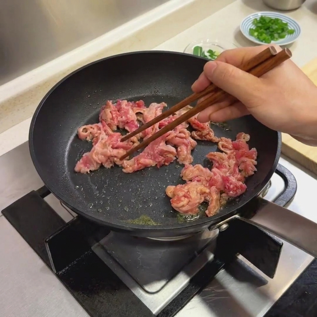 Mariniertes Rindfleisch wird in einer schwarzen Bratpfanne mit Holstäbchen gekocht.