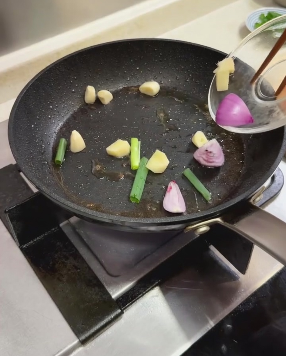 Frühlingszwiebelstücke, Knoblauchzehen und geschnittene rote Zwiebeln werden in einer heißen Bratpfanne angebraten.