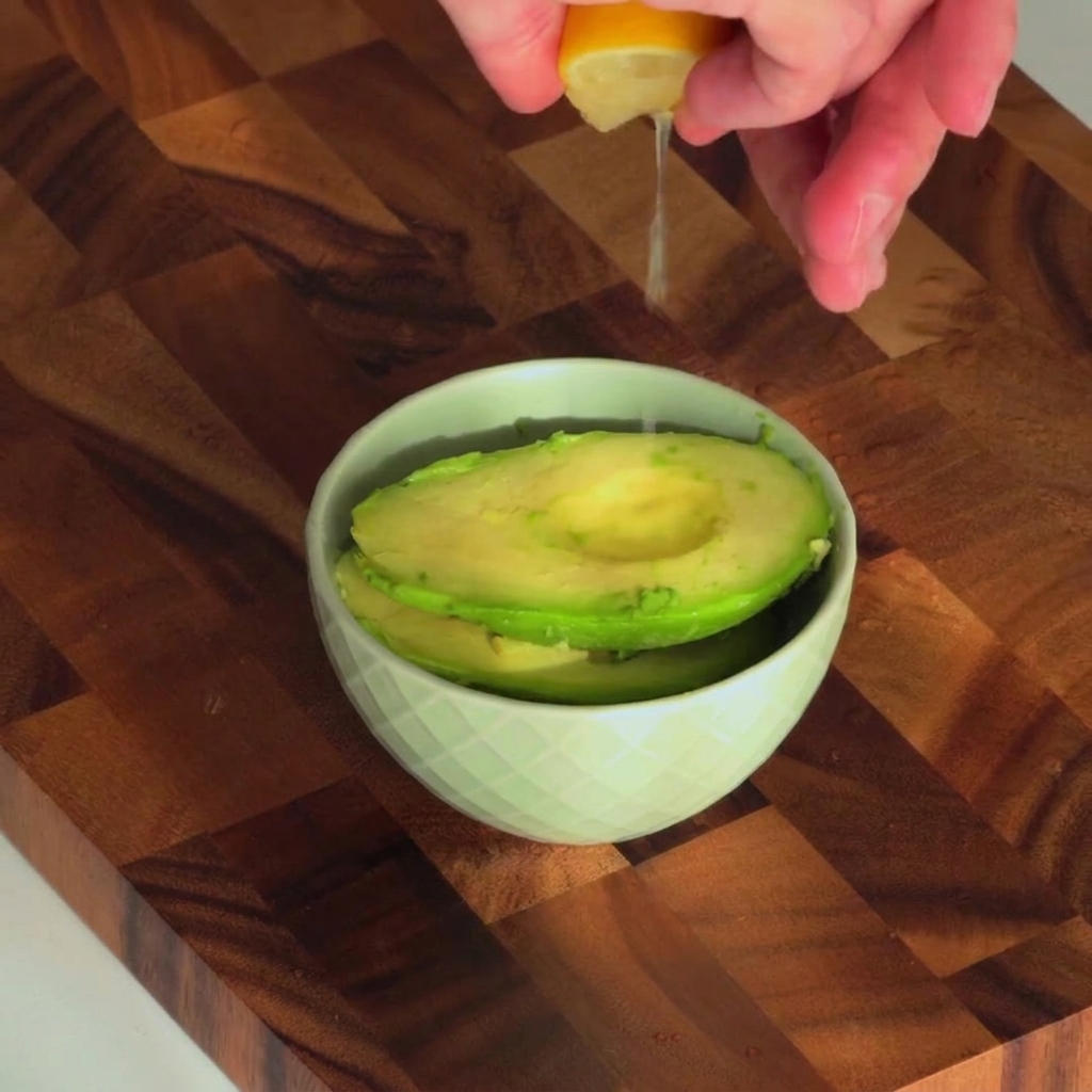 Frischer Zitronensaft wird in eine kleine Schüssel mit ausgehöhlter Avocado geträufelt.