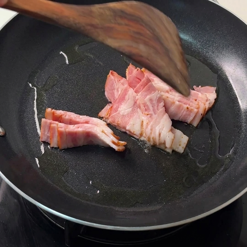 Speckstreifen braten in einer heißen schwarzen Pfanne, während ein Holzspatel sie wendet.