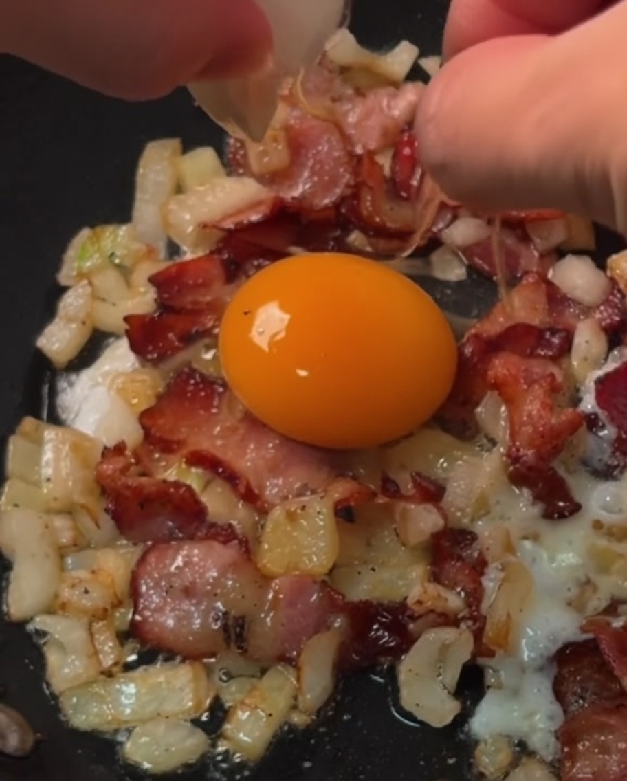 Frische Eier braten in einzelnen Speck- und Zwiebelringen in einer Pfanne.