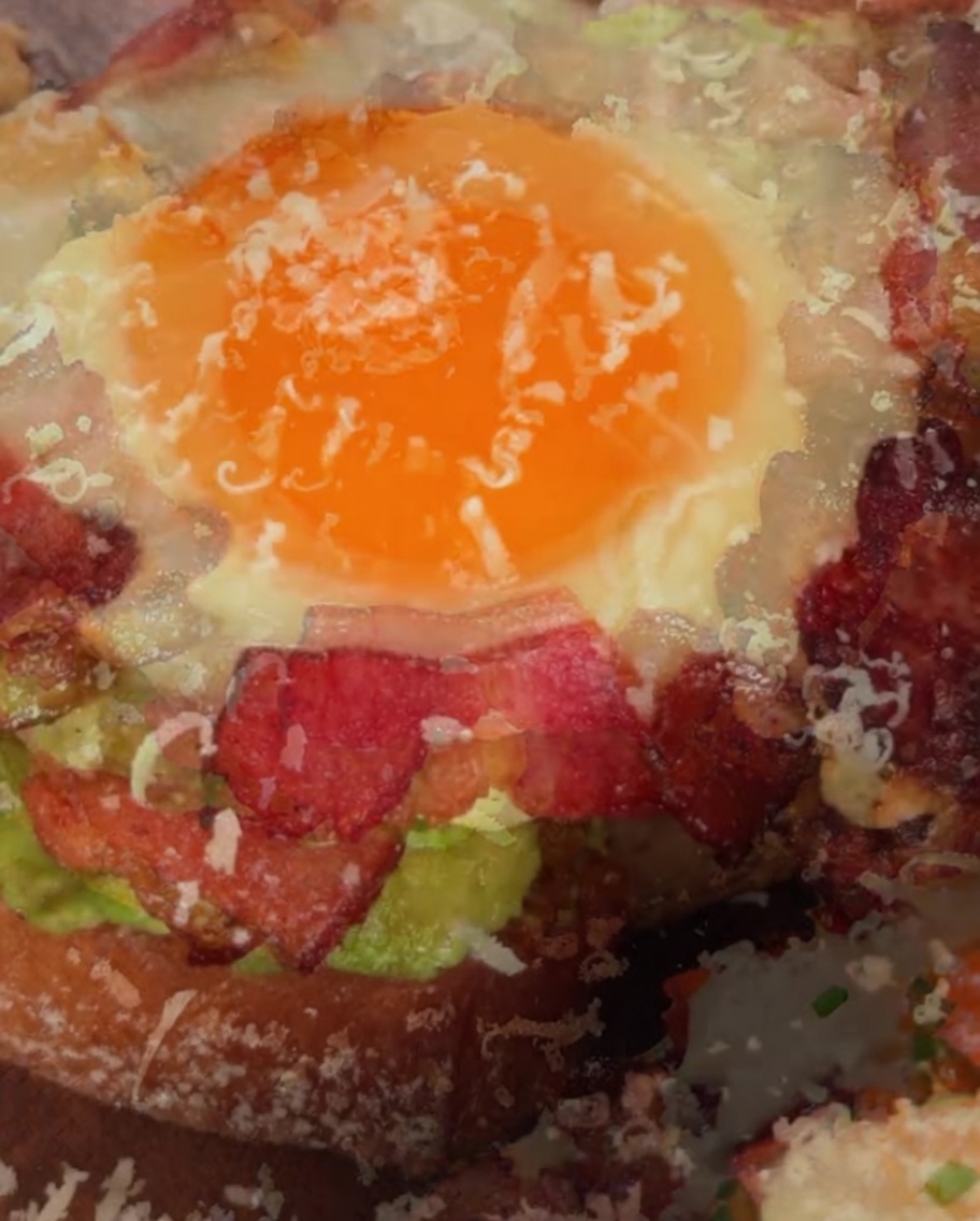 Geriebener Parmesan wird auf die Oberseite eines fertigen Avocado-Ei-Sandwiches gestreut.