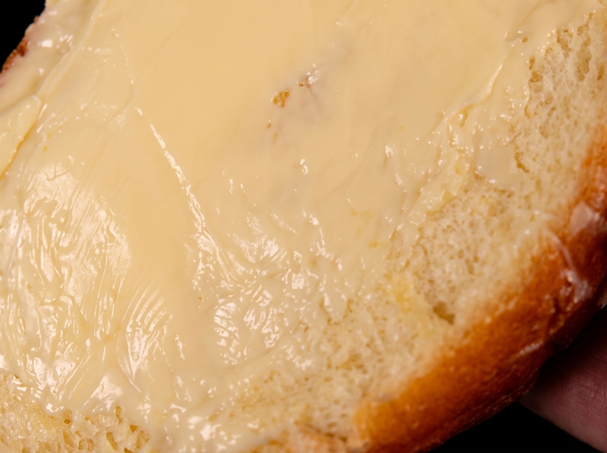 Eine einzelne, mit Butter bestrichene Brotscheibe liegt mit der gebutterten Seite nach unten in einer heißen Pfanne.