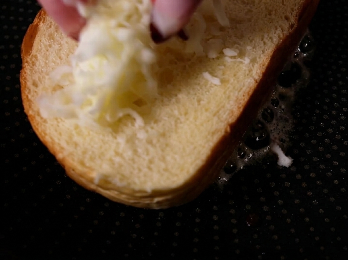 Finger, die geriebenen Mozzarella auf eine einfache Brotscheibe in einer heißen Pfanne streuen.
