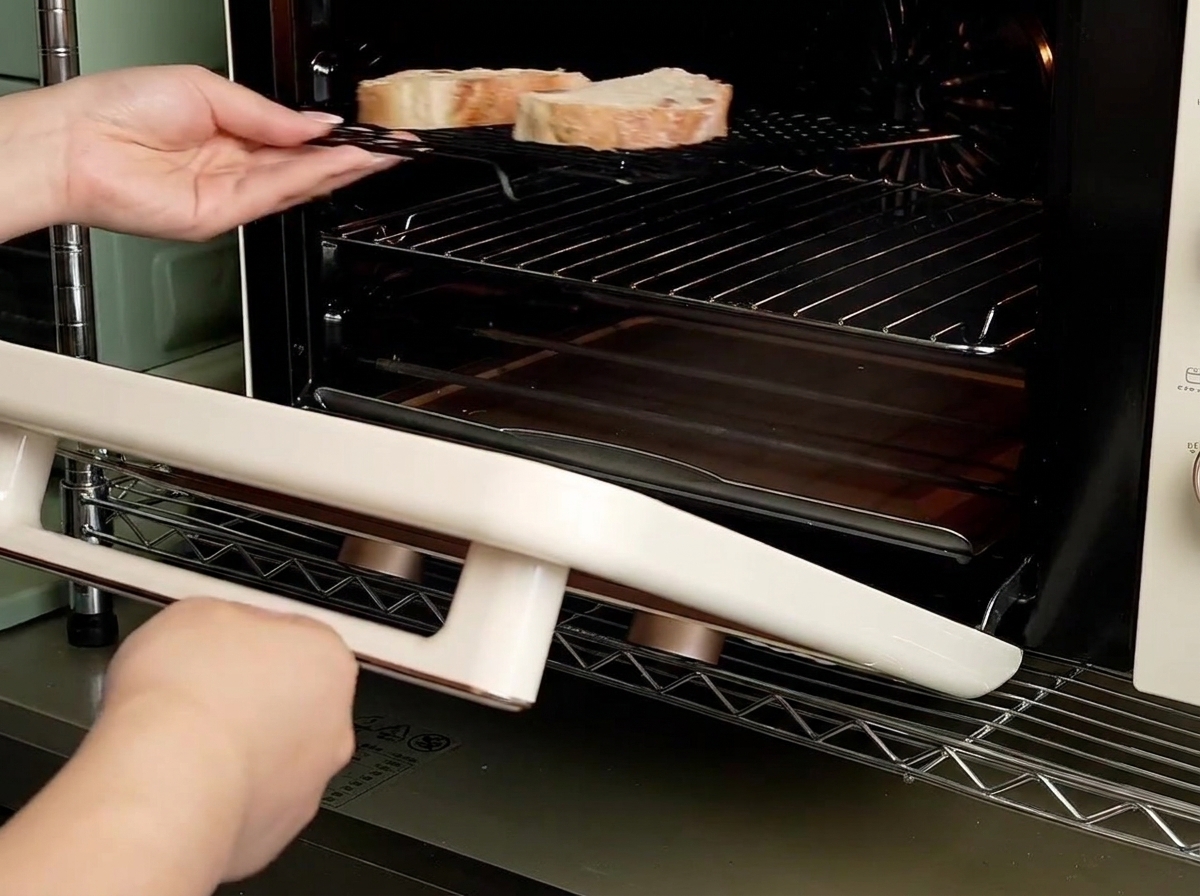 Hände schieben ein Kuchengitter mit zwei Brotscheiben in einen kleinen Mini-Backofen.