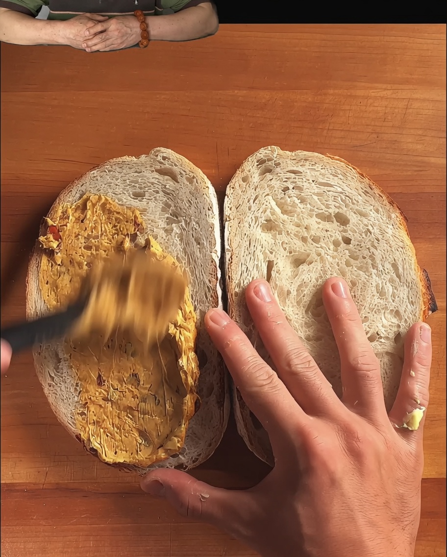 Scheiben rustikalen Sauerteigbrots mit einer reichhaltigen Sauce, die mit einem Löffel glattgestrichen wird.