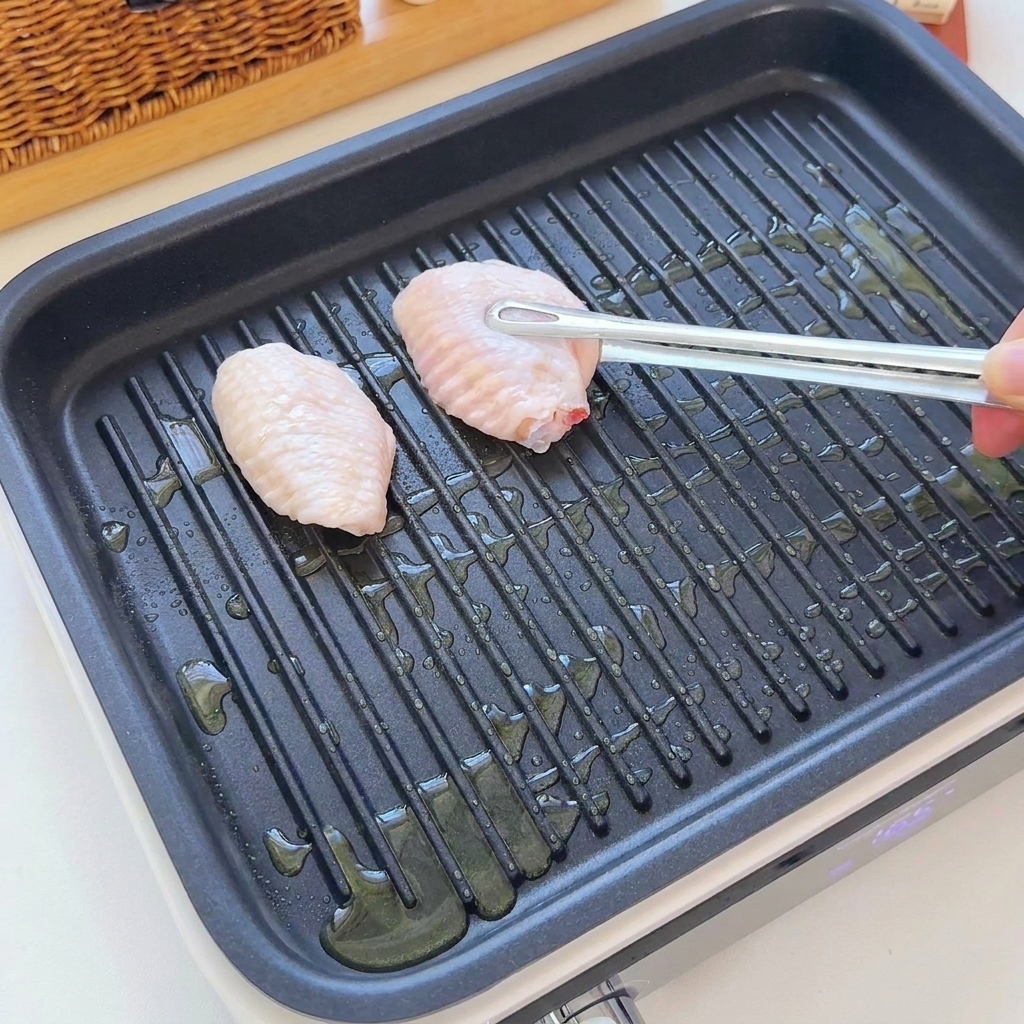 Rohe Hähnchenflügel werden mit einer Zange auf eine gerippte Grillpfanne mit Öl gelegt.