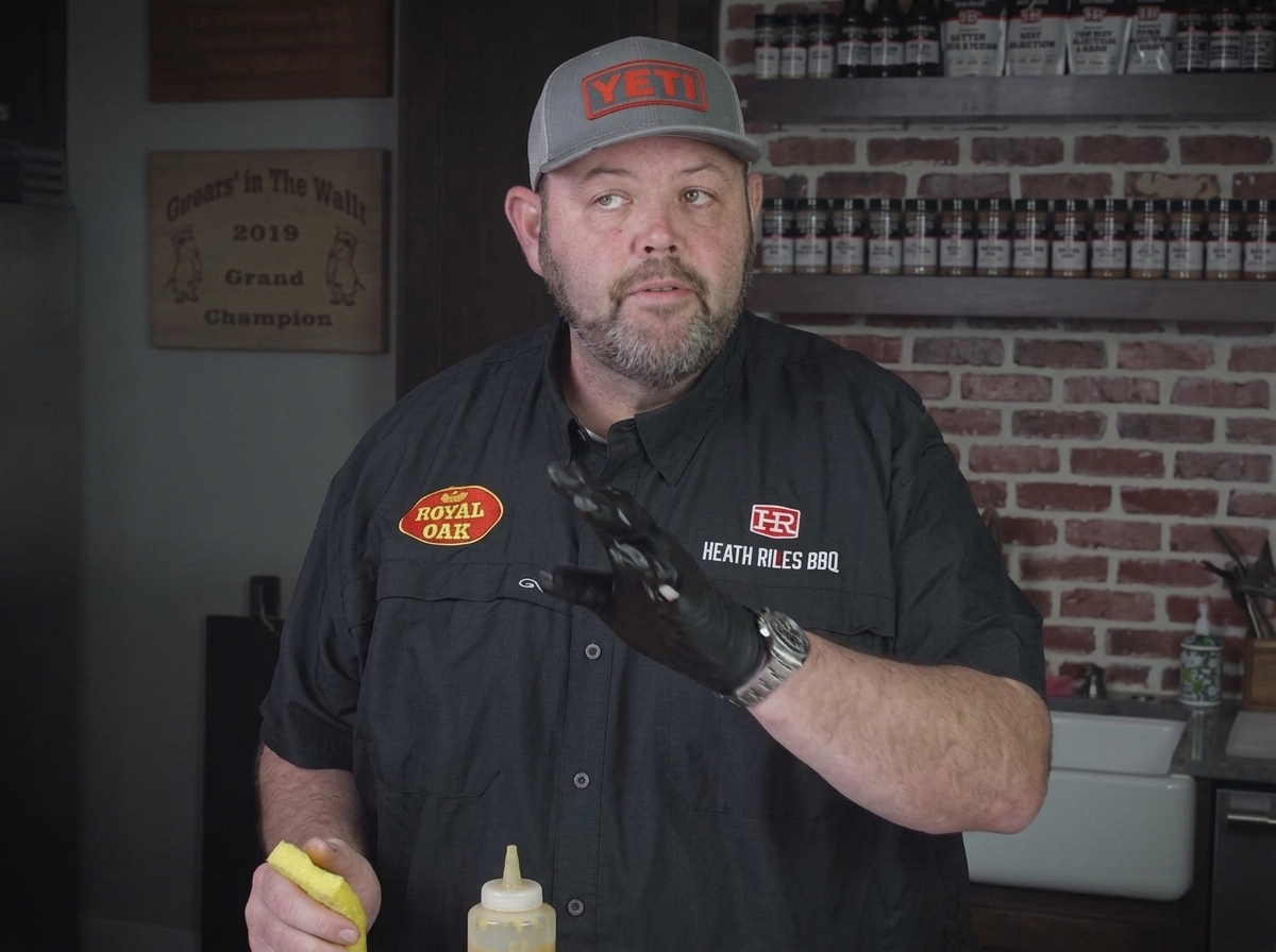 Gelber Senf wird aus einer Flasche auf rohe Schweinerippchen gedrückt, um als Würzbinder zu dienen.