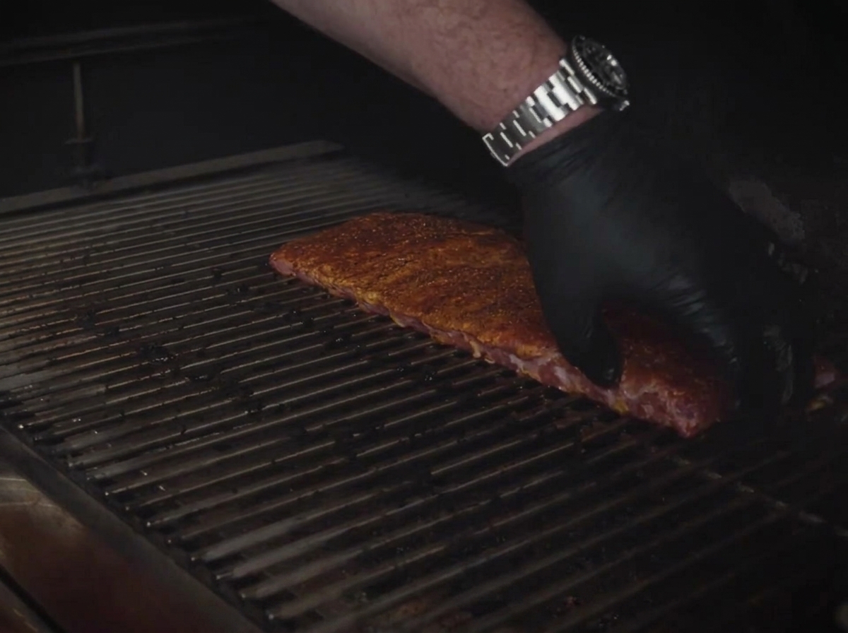 Gewürzte St. Louis Ribs werden flach auf die Metall-Garklammern eines Smokers gelegt.