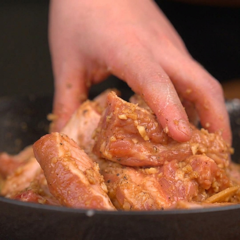 Eine Hand mischt und massiert rohe Schweinerippchen mit einer dicken, würzigen Knoblauchmarinade in einer Schüssel.