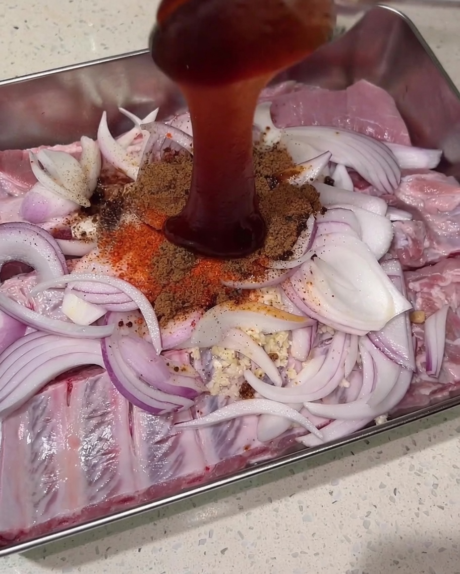 Dicke, dunkelrote Char-Siu-Sauce wird von oben auf das Gewürz-, Rippchen- und Zwiebelbett gegossen.