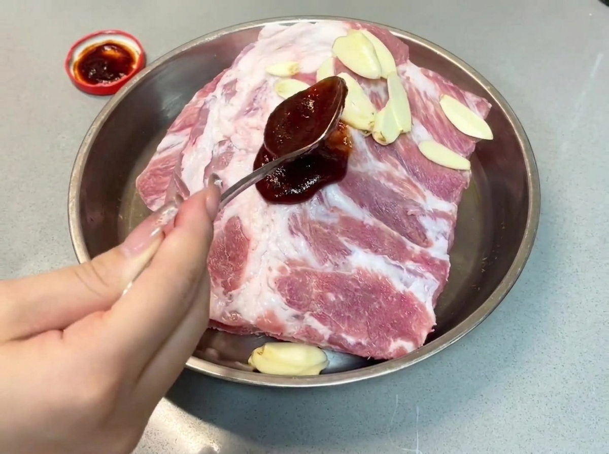 Ein Löffel dunkle Char-Siu-Soße wird auf Schweinerippchen in einer Metallschale gegeben.