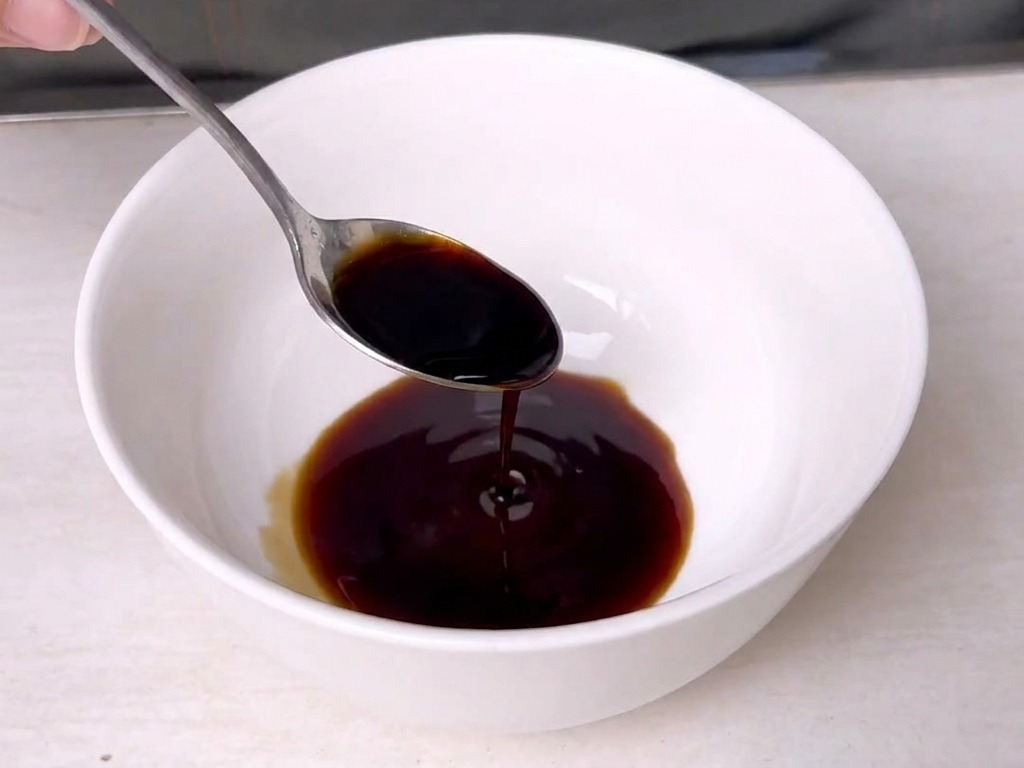 Ein Metalllöffel rührt eine dunkle, sämige Sauce in einer kleinen weißen Keramisschüssel um.