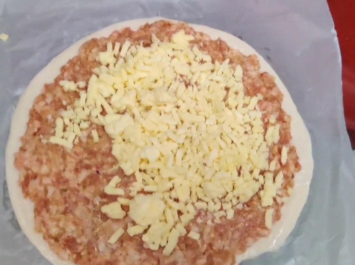 Giebter gelber Käse gehäuft auf einer Schicht rohem Hackfleisch auf einem Frühlingszwiebelpfannkuchen.