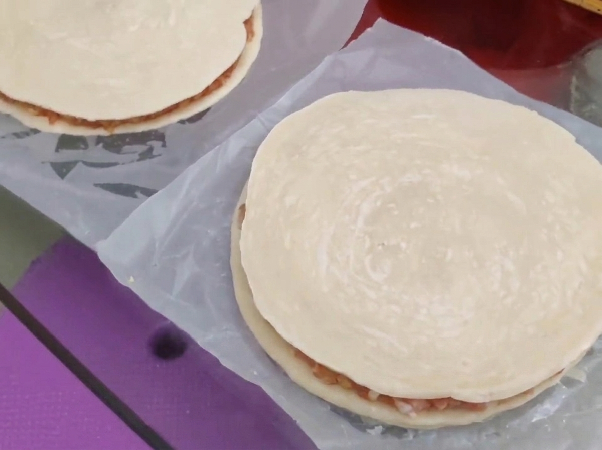 Ein zweiter runder Frühlingszwiebelpfannkuchen wird über die Fleisch- und Käsefüllung gelegt, um einen geschlossenen Kuchen zu formen.