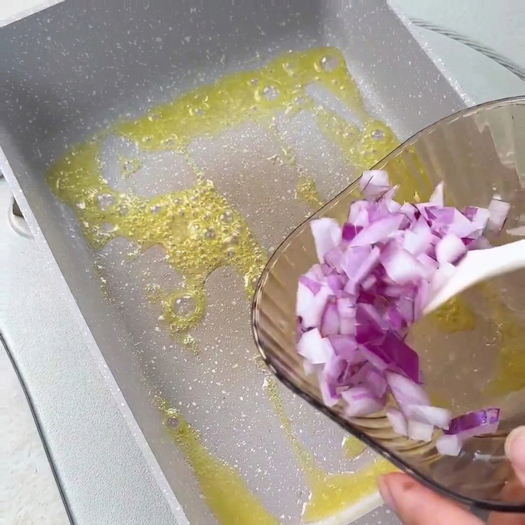 Gehackte rote Zwiebeln werden aus einer Glasschüssel in geschmolzene Butter in einer eckigen Pfanne gegeben.