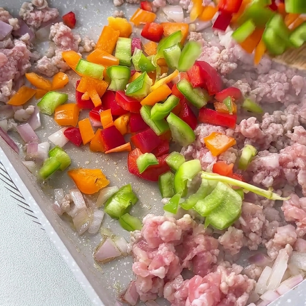 Gewürfelte rote, gelbe und grüne Paprika wird in die Pfanne zur Fleischmischung gegeben.