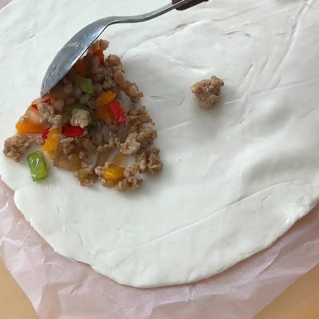 Ein Löffel gekochte Fleischfüllung wird auf ein rundes Fladenbrotteigblatt auf Backpapier platziert.