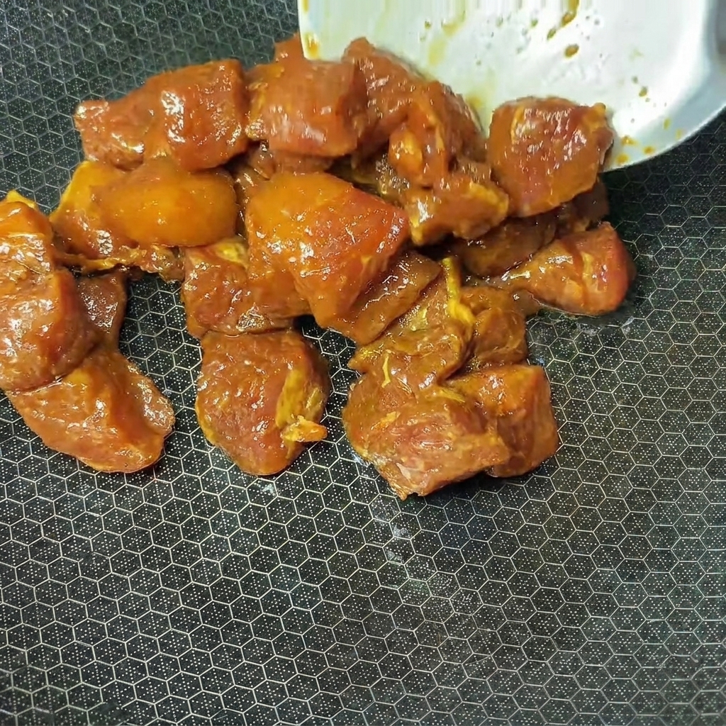 Marinierte Schweinefleischwürfel werden zum Garen in einen heißen Wok gegeben.