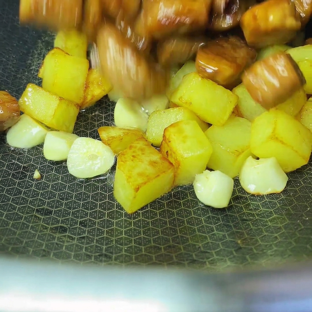 Gekochte Kartoffeln und Schweinefleisch werden in einem Wok zusammengeführt.
