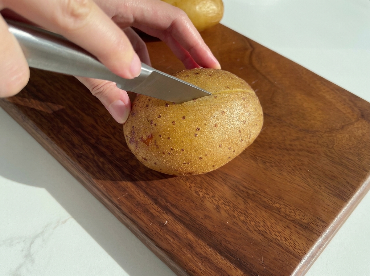 Ein Messer schneidet eine gebackene Kartoffel auf einem Holzbrett durch.