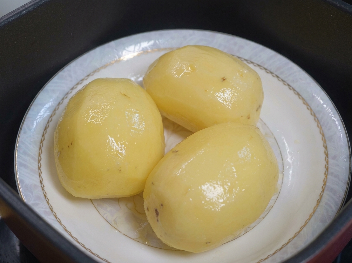 Gedämpfte Kartoffeln auf einem Teller, bereit, mit Öl bestrichen zu werden.