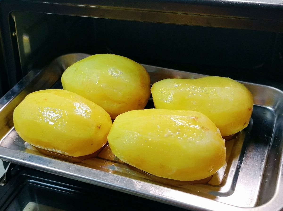 Ein Metallblech mit geölten ganzen Kartoffeln wird in einen kleinen schwarzen Ofen geschoben.