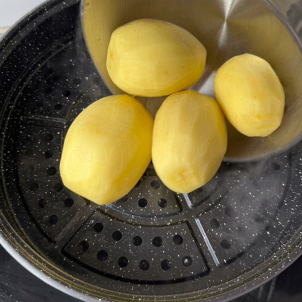 Geschälte gelbe Kartoffeln werden auf einen Dämpfeinsatz über kochendem Wasser gelegt.