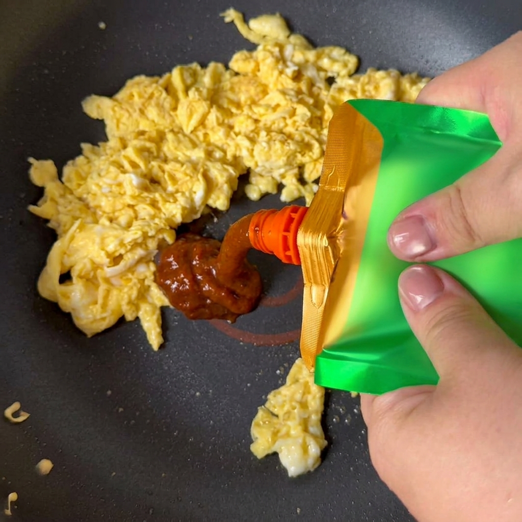Gelbe Sojabohnenpaste wird aus einem Beutel auf das Rührei in der Pfanne gedrückt.