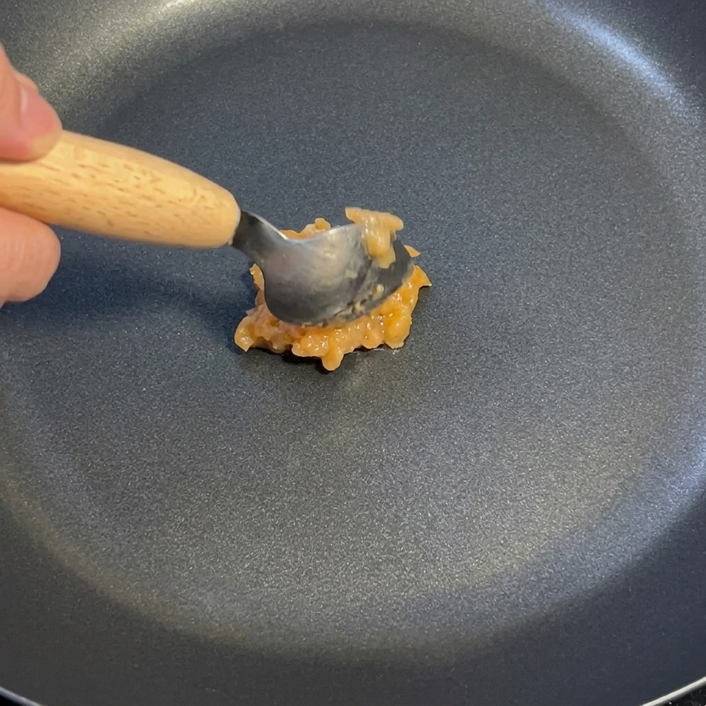 Ein Löffel Knoblauch-Ingwer-Sauce wird in einer dunklen Antihaftpfanne bei schwacher Hitze umgerührt.
