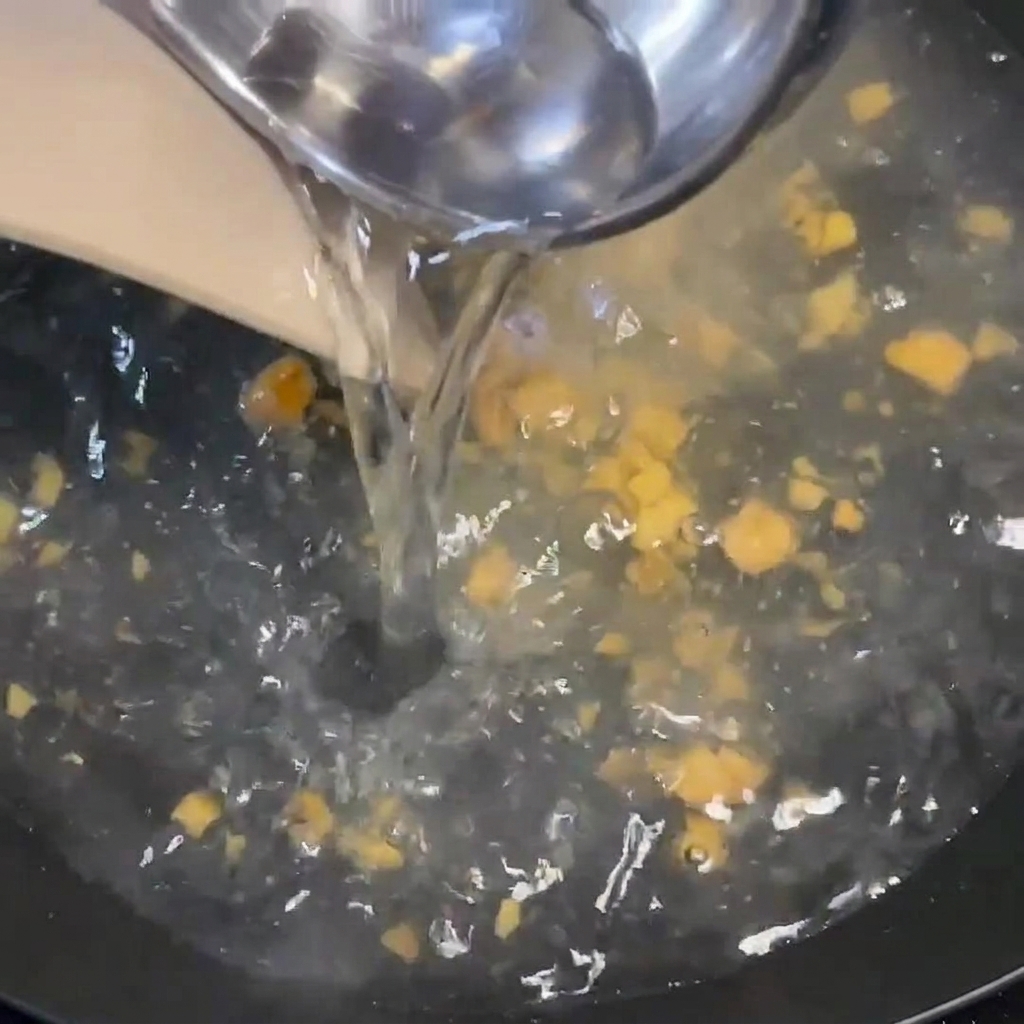 Heißes Wasser wird aus einer Kelle in einen kochenden Topf mit Gewürzen und Ingwerstücken gegossen.