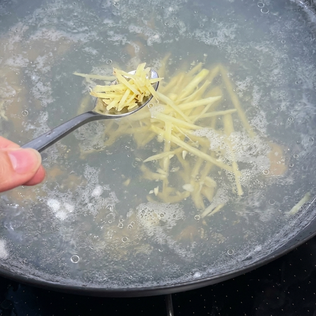 Ein Löffel Ingwerstreifen wird in einen kochenden Topf mit klarer Suppenbrühe gegeben.