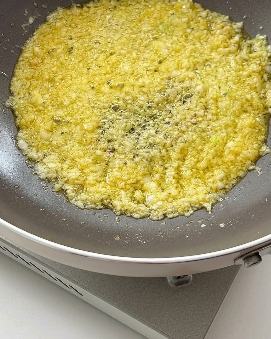 Sojasauce und Austernsauce werden in die brutzelnde Knoblauch-Butter-Mischung in einer Pfanne gegossen.