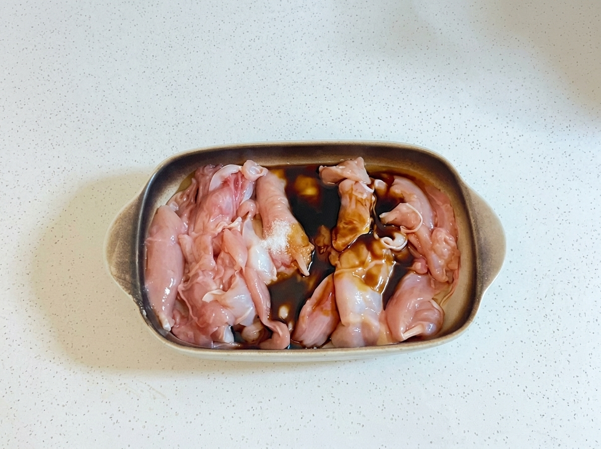 Dunkle Kochflüssigkeiten und Öl werden über rohe Hähnchenstücke in einer Auflaufform gegossen.