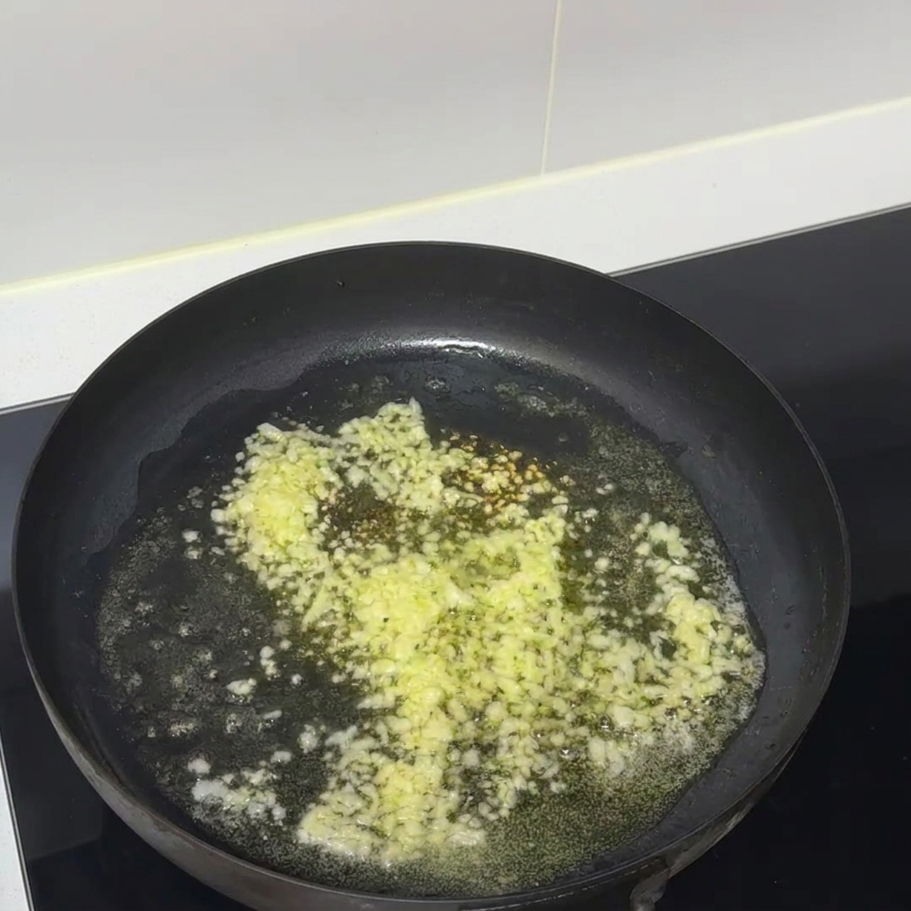 Gehackter Knoblauch und geschmolzene Butter zischen zusammen in einer schwarzen Antihaft-Bratpfanne.
