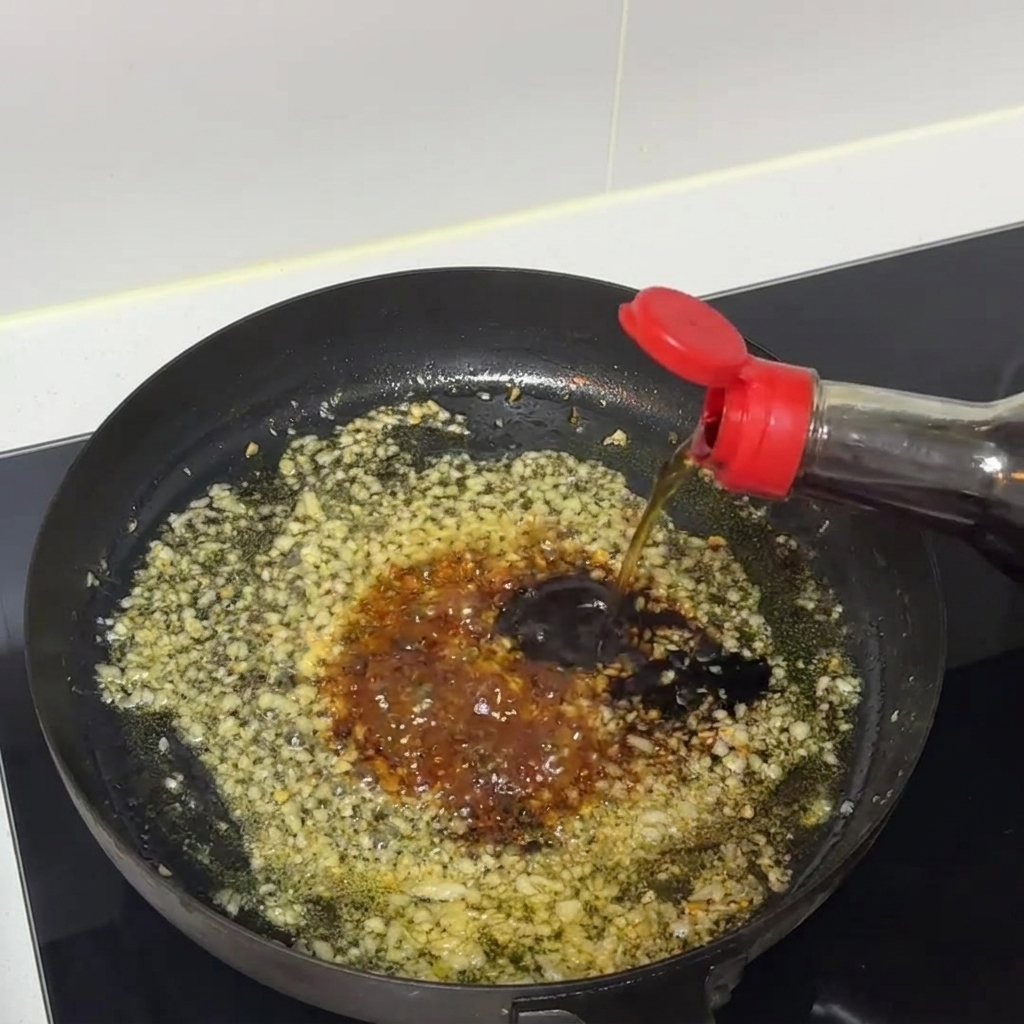 Dunkle Saucenmischung köchelt und wird in einer Bratpfanne mit gehacktem Knoblauch umgerührt.
