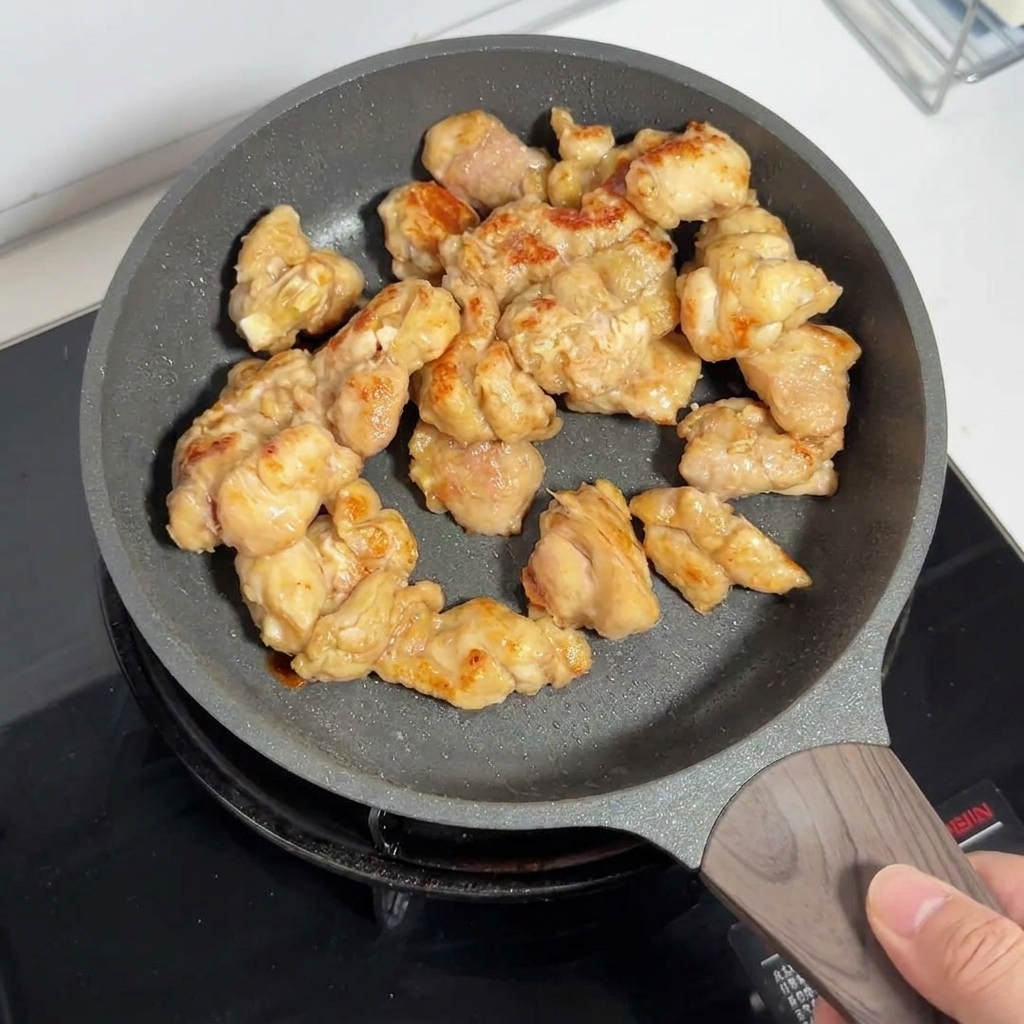 Goldbraune Hähnchenschenkelstücke braten in einer Antihaft-Pfanne.