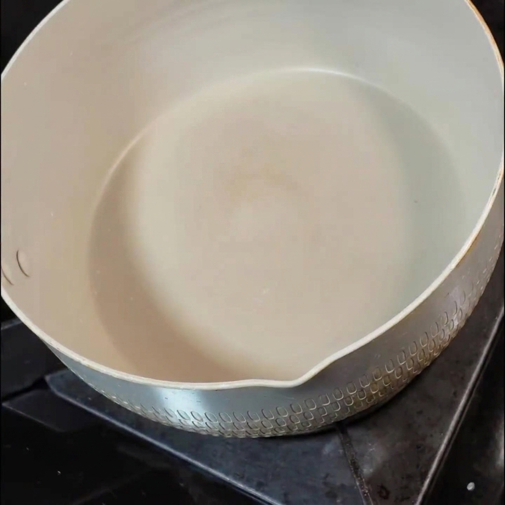 Ein kleines Stück Butter schmilzt in einer weißen Keramikpfanne auf einer Herdplatte.