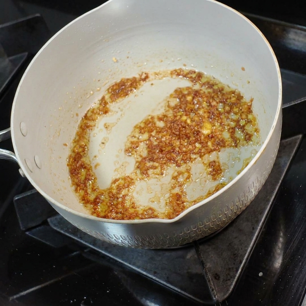 Eine kleine Kelle herzhafte Nudelsuppe wird in die aromatische Knoblauch-Butter-Mischung gegossen.