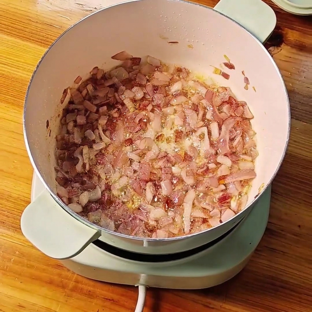 Angebratene gewürfelte rote Zwiebeln in einem Topf werden mit gehacktem Knoblauch und Ingwer vermischt.cite: 1