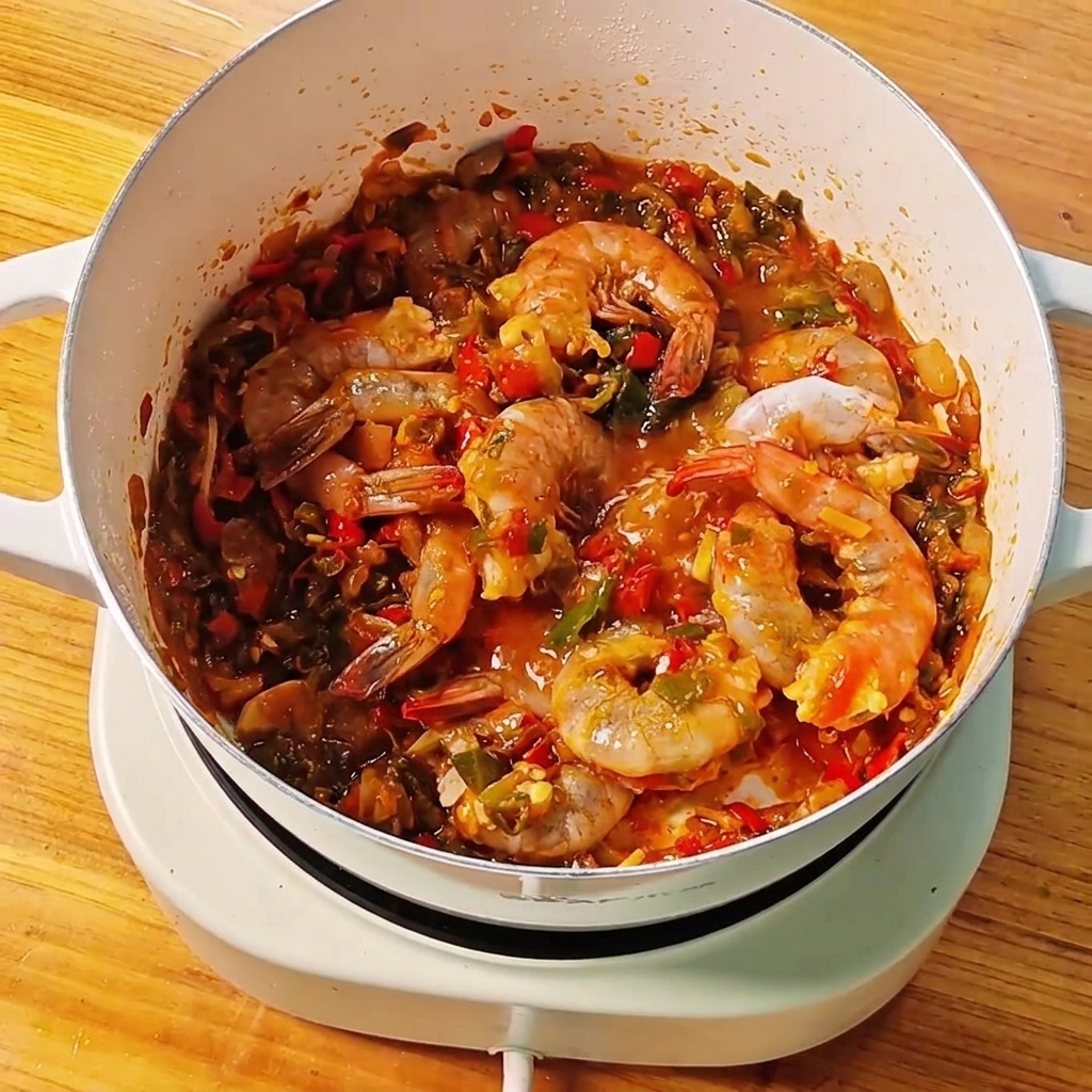 Klares Wasser wird aus einer kleinen Schüssel in einen Topf mit Garnelen und Sauce gegossen.cite: 1