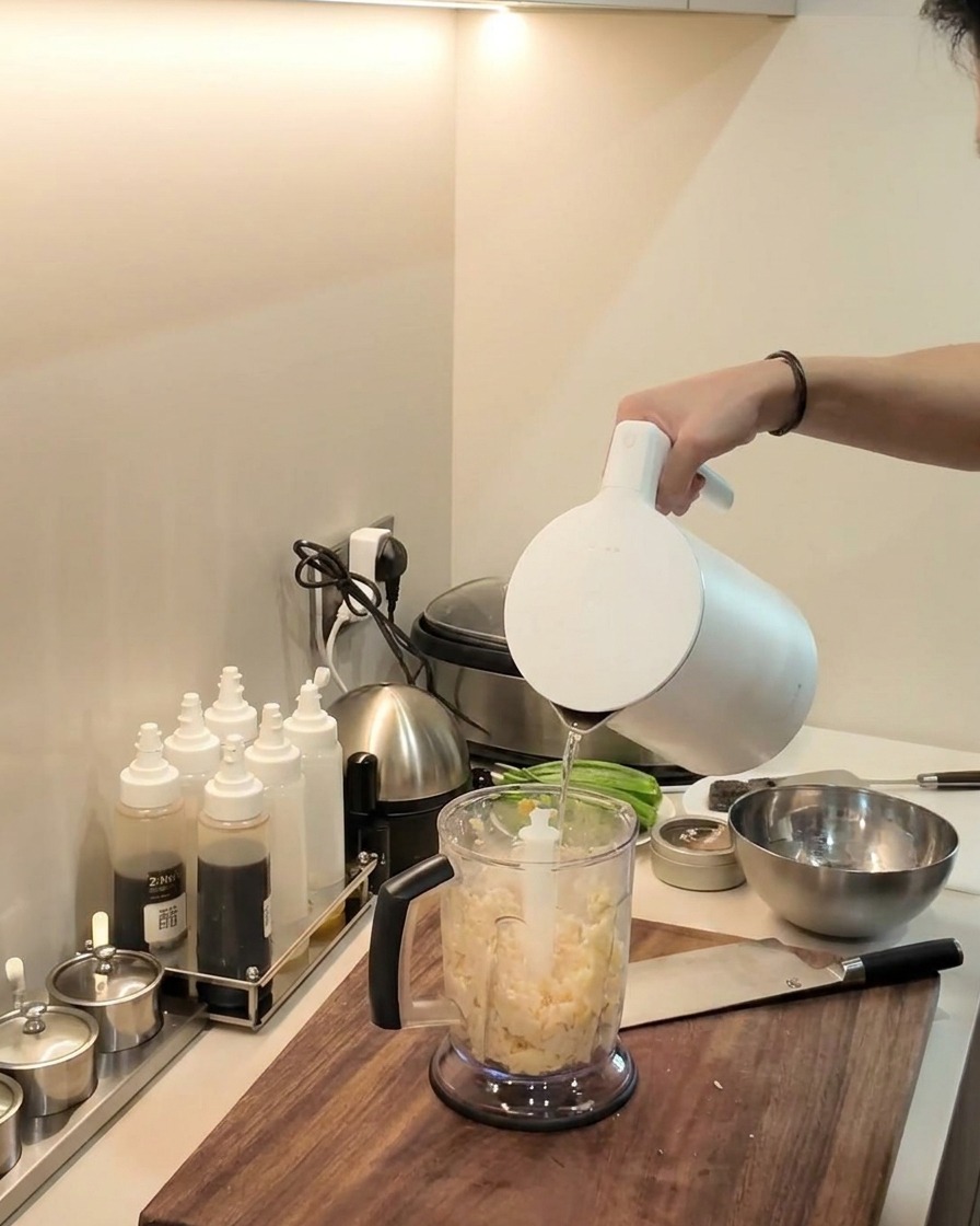 Ein Stabmixer püriert die Maniok- und Kochbananenmischung im Mixerbehälter.