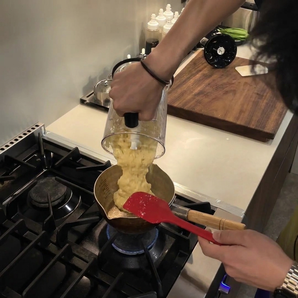 Das glatte, blassgelbe Püree wird aus einem Mixerbehälter in einen kleinen Metalltopf auf einem Gasherd gegossen.
