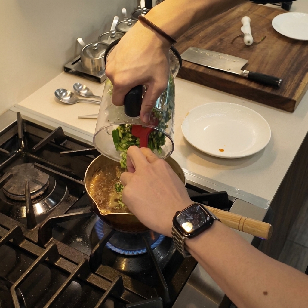 Zerkleinerter grüner Okra wird mit einem roten Spatel aus einem Mixerbecher in einen Topf mit köchelndem Eintopf geschabt.