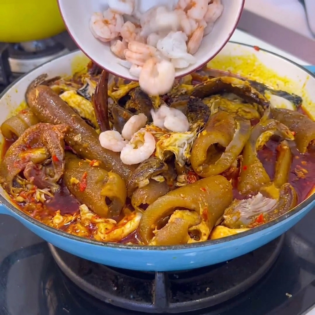 Eine Schüssel geschälter weißer Garnelen wird in einen Kochtopf mit geschmorter Schweinehaut und Chilisauce gegeben.