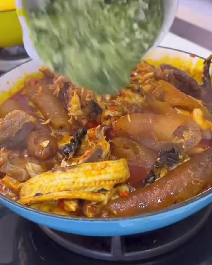 Fein gehackte grüne Okra wird aus einer weißen Schüssel in einen reichhaltigen, blubbernden Topf mit Fleisch und Sauce geschüttet.