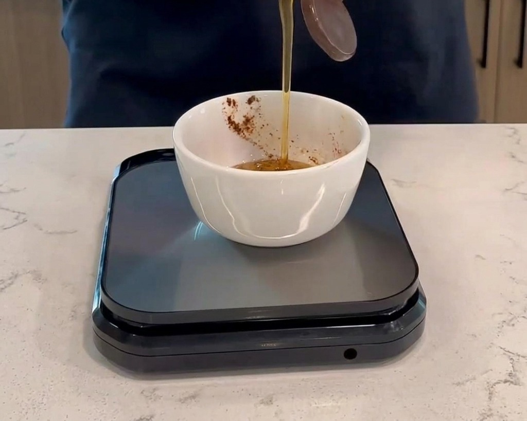 Honig wird aus einer Plastikflasche in eine kleine weiße Schüssel mit dunkelroter Sauce gegossen, die auf einer schwarzen digitalen Küchenwaage steht.