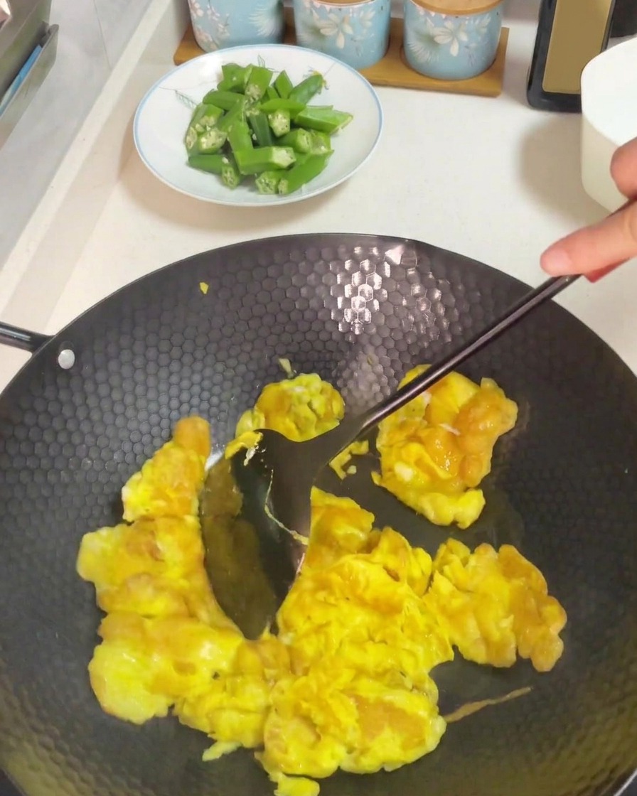 Mit einem dunklen Pfannenwender werden die garenden Eier in einem heißen Wok verrührt.