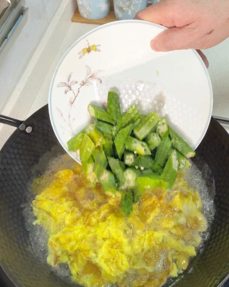 Frisch geschnittene grüne Okrastücke werden in einen Wok mit blubbernder Eiersuppe gegeben.